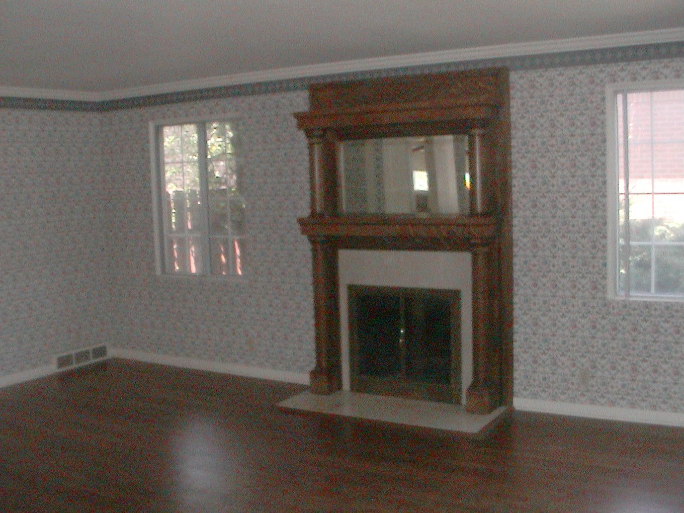 Living room before renovation with patterned wallpaper and a dated fireplace surround