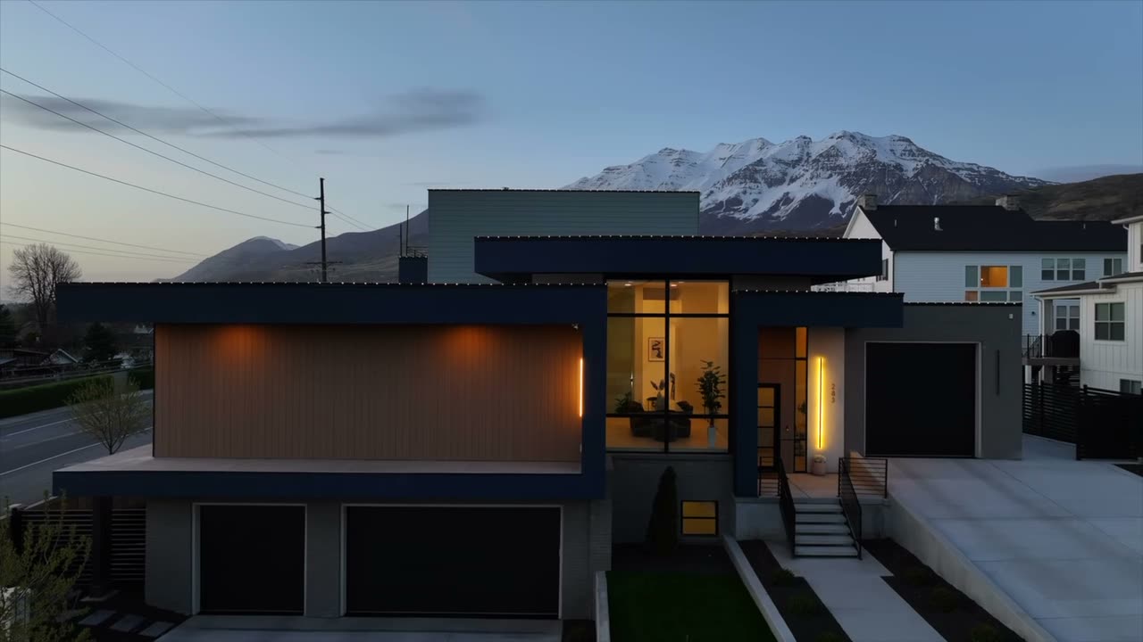 Modern home at dusk with dark cladding, wood soffit, and a snow-capped mountain behind it
