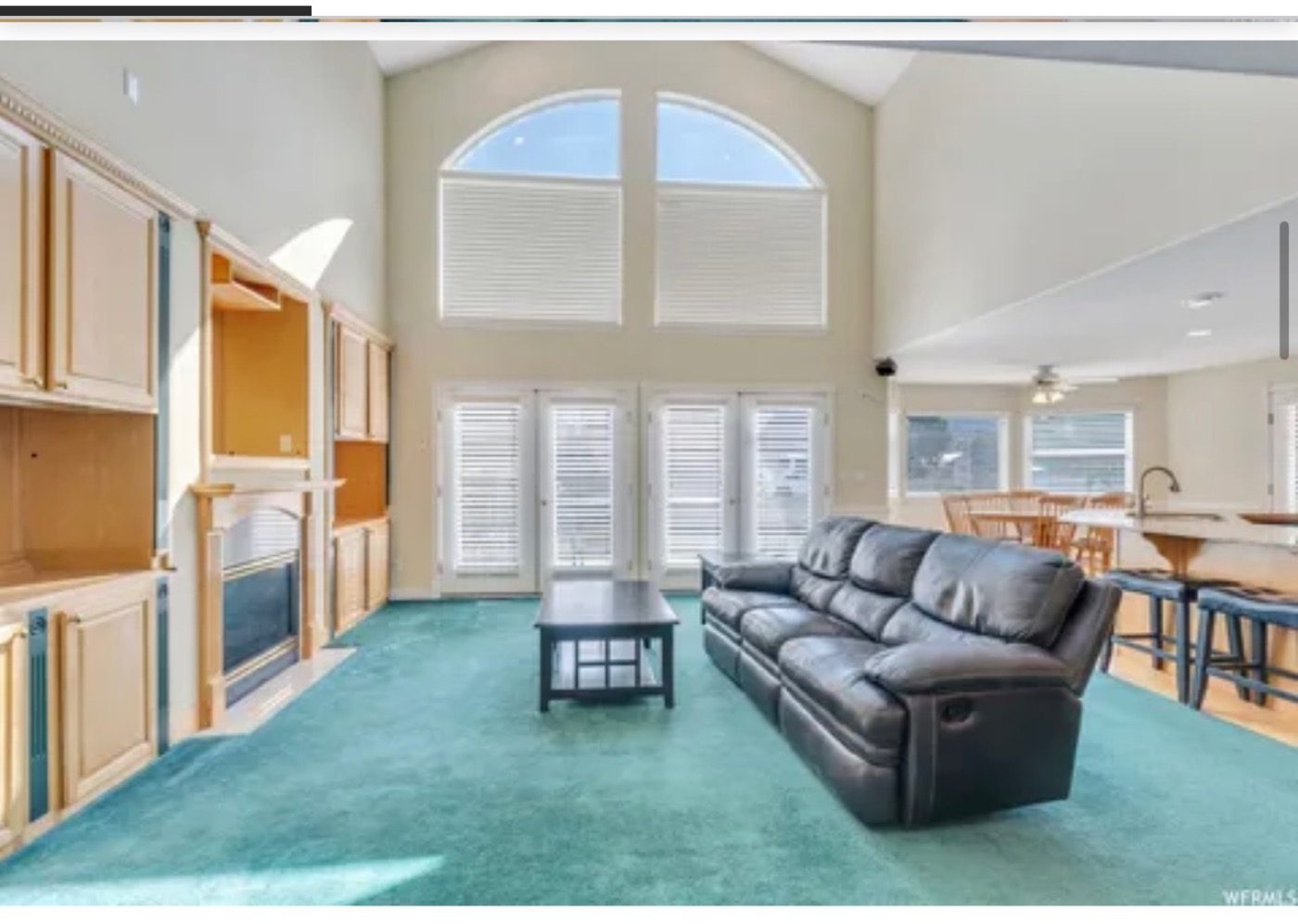 A vaulted living room with green carpet and a dated fireplace before the renovation